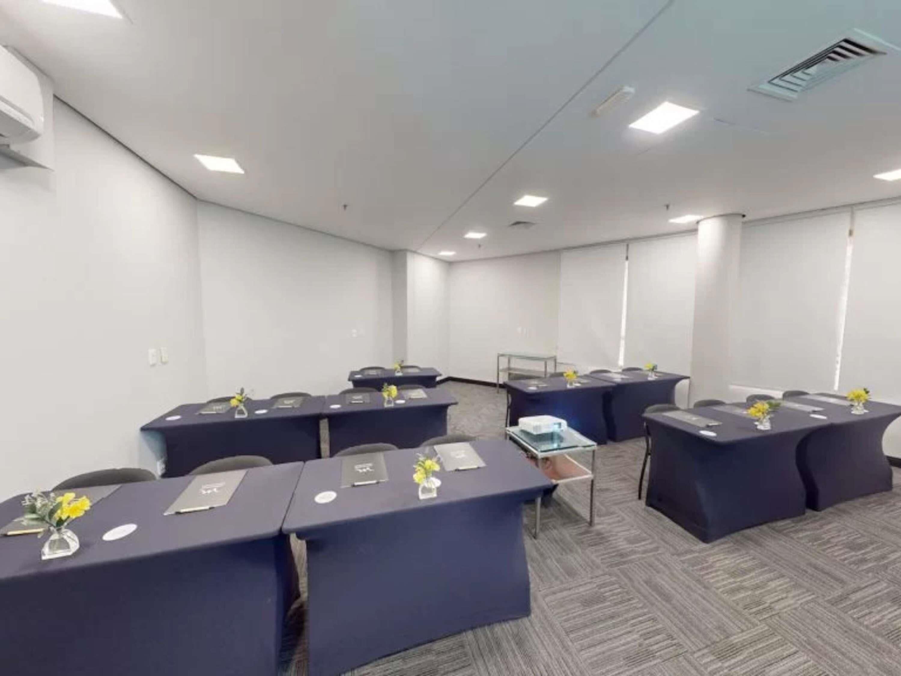Uma sala de conferências com várias mesas, cadeiras e um projetor.