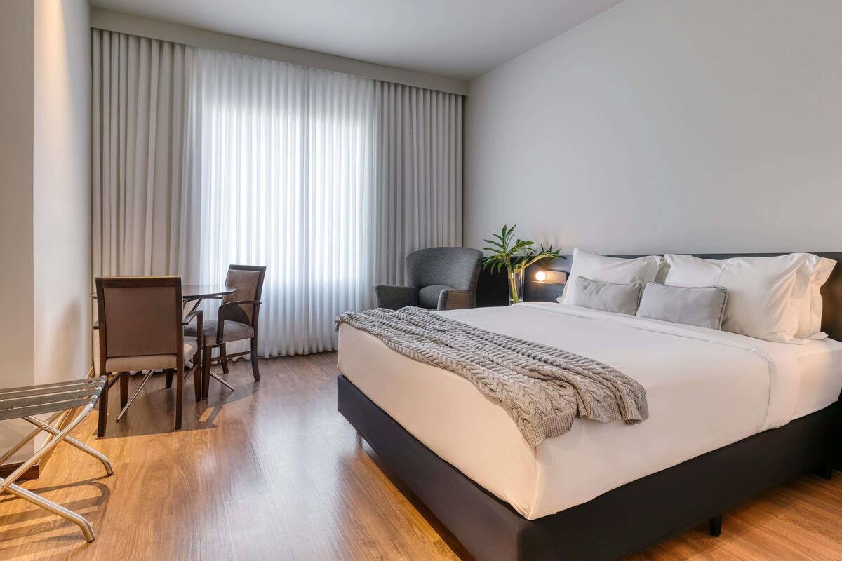 A modern hotel room with a large bed, a desk, a chair, and a potted plant.