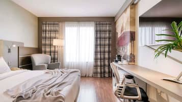 Habitación de hotel con cama, escritorio, silla y una planta grande.
