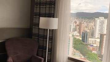 A room with a view of a cityscape through a window, a floor lamp, and a chair.