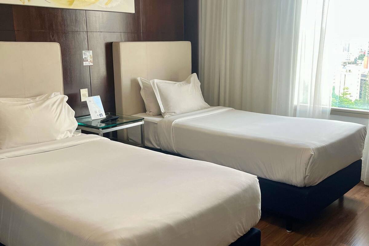 A hotel room with two beds, a small table with a phone, and a window with curtains.