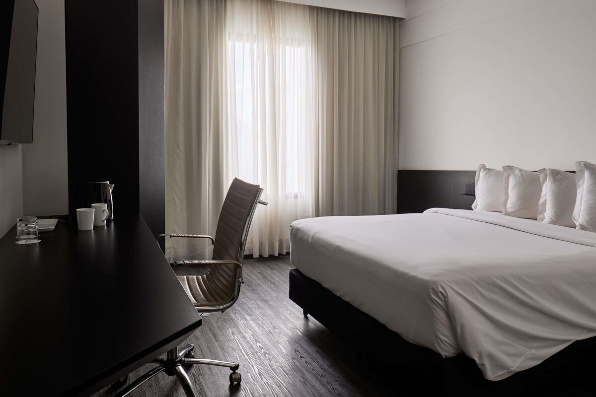 A hotel room with a bed, a desk, a chair, and a large window with curtains.
