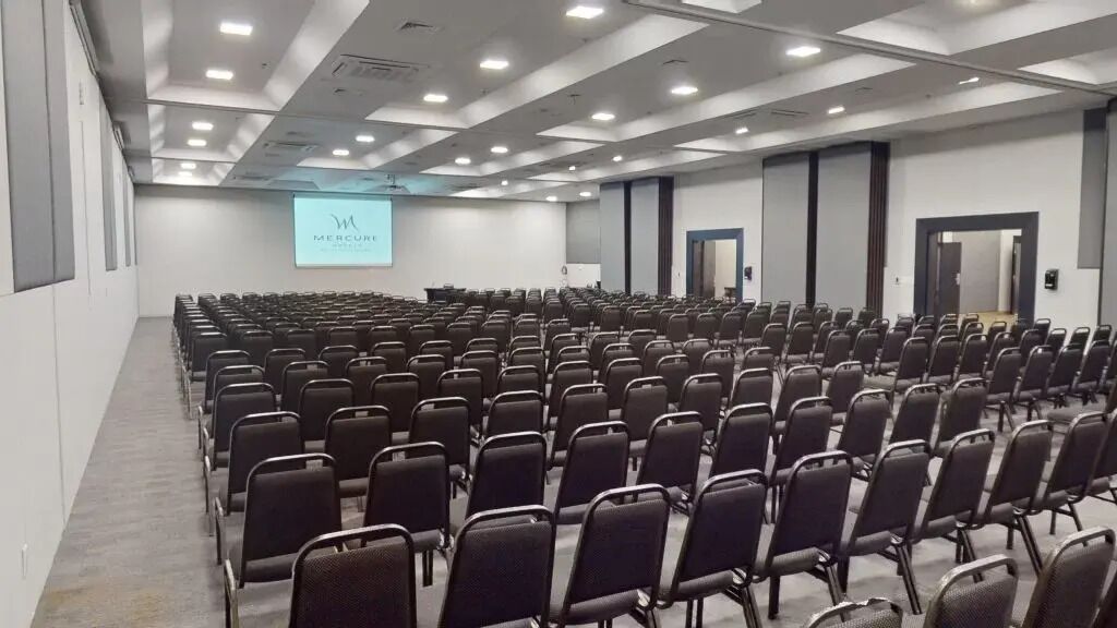 A conference room with rows of chairs, a projection screen, and a stage area.