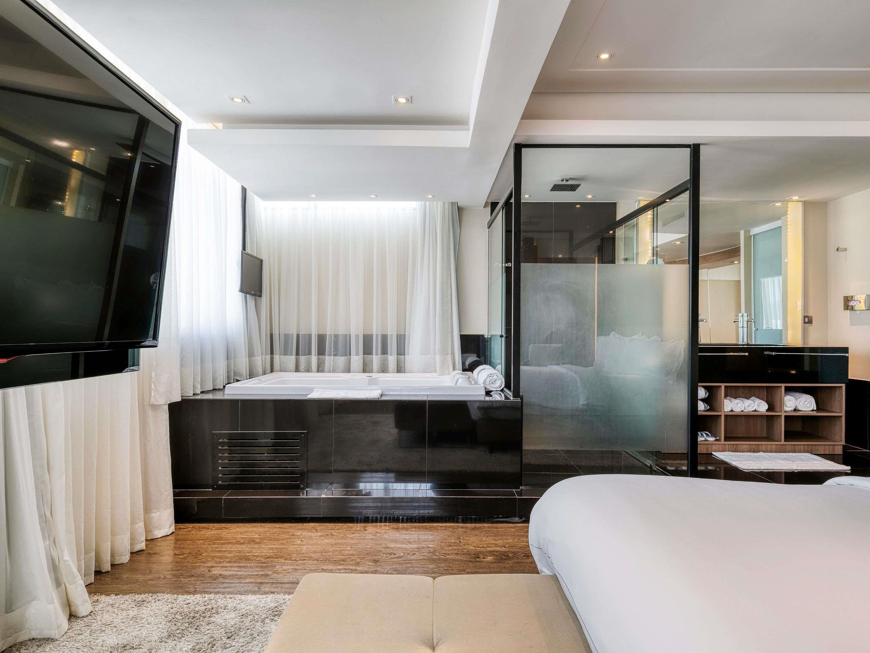 Une chambre à coucher moderne avec un grand lit, une douche en verre, un téléviseur à écran plat et un plancher en bois.