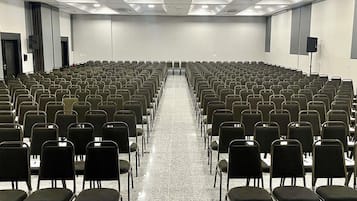 Une salle de conférence avec des rangées de chaises, un plancher ciré et des luminaires au plafond.