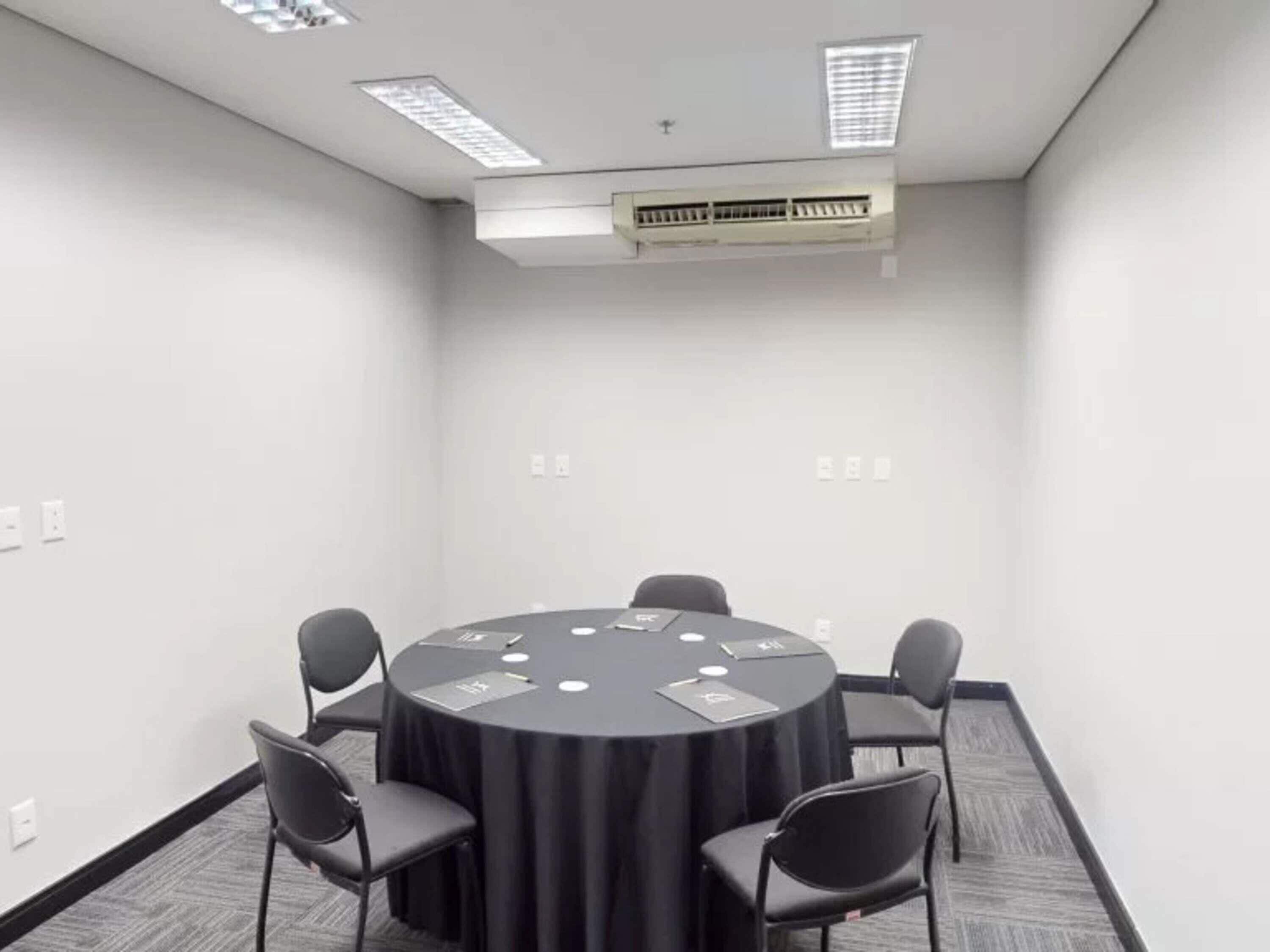 A conference room with a round table, six chairs, and a ceiling-mounted air conditioning unit.