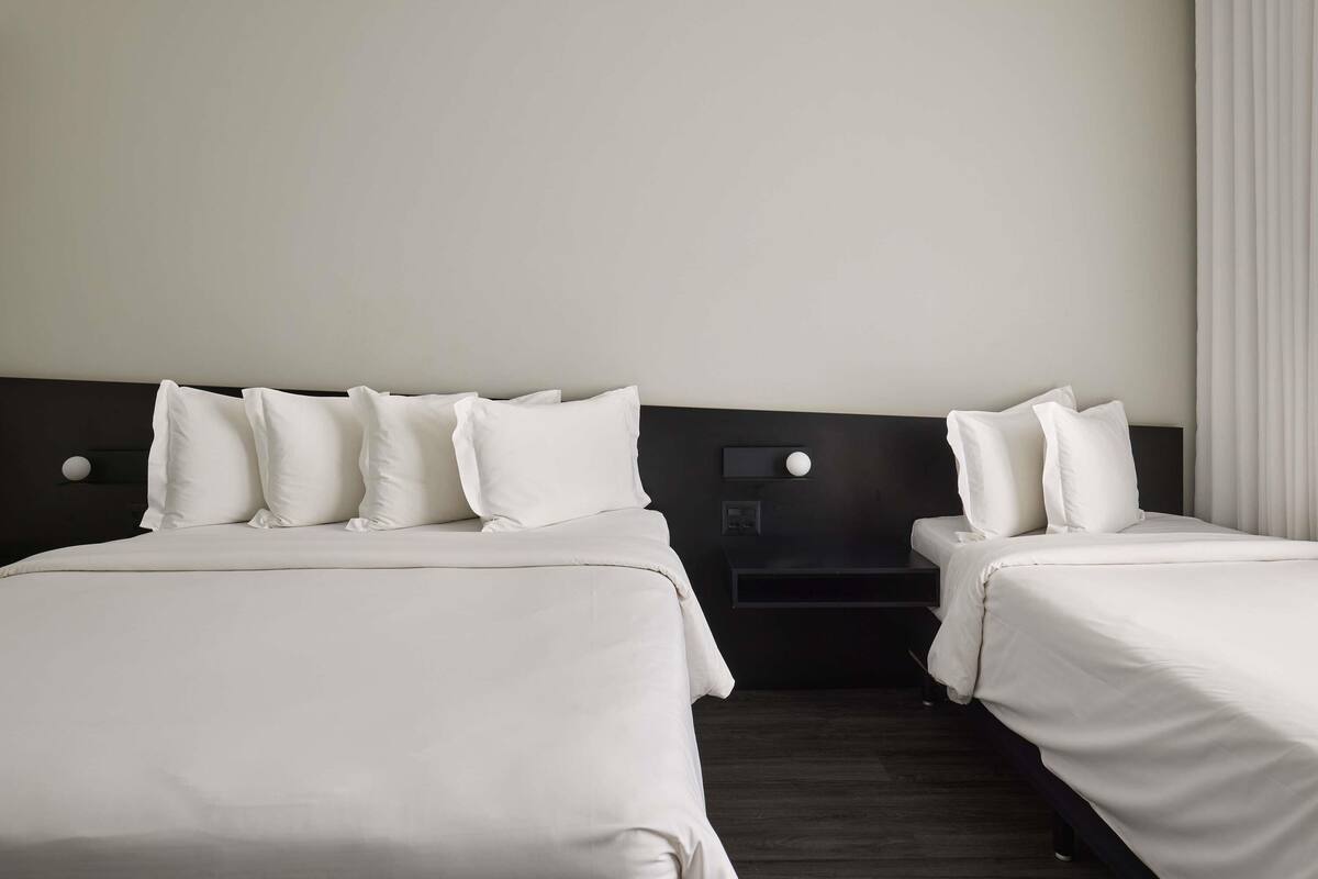 A hotel room with two beds, a dark headboard, a nightstand, and a wall-mounted control panel.