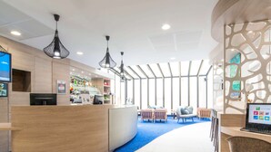 A modern reception area with a curved wooden reception desk, multiple seating options, and a large window providing natural light. - ibis Styles La Rochelle Centre Vieux Port (La Rochelle)