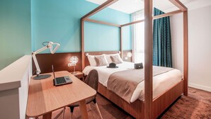 A hotel room with a four-poster bed, a desk with a laptop, a bedside lamp, and a nightstand. - ibis Styles La Rochelle Centre Vieux Port (La Rochelle)