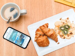 A white plate with croissants, sliced apples, and kiwi slices, a cup of coffee, and a smartphone displaying a camera app. - ibis Styles La Rochelle Centre Vieux Port (La Rochelle)