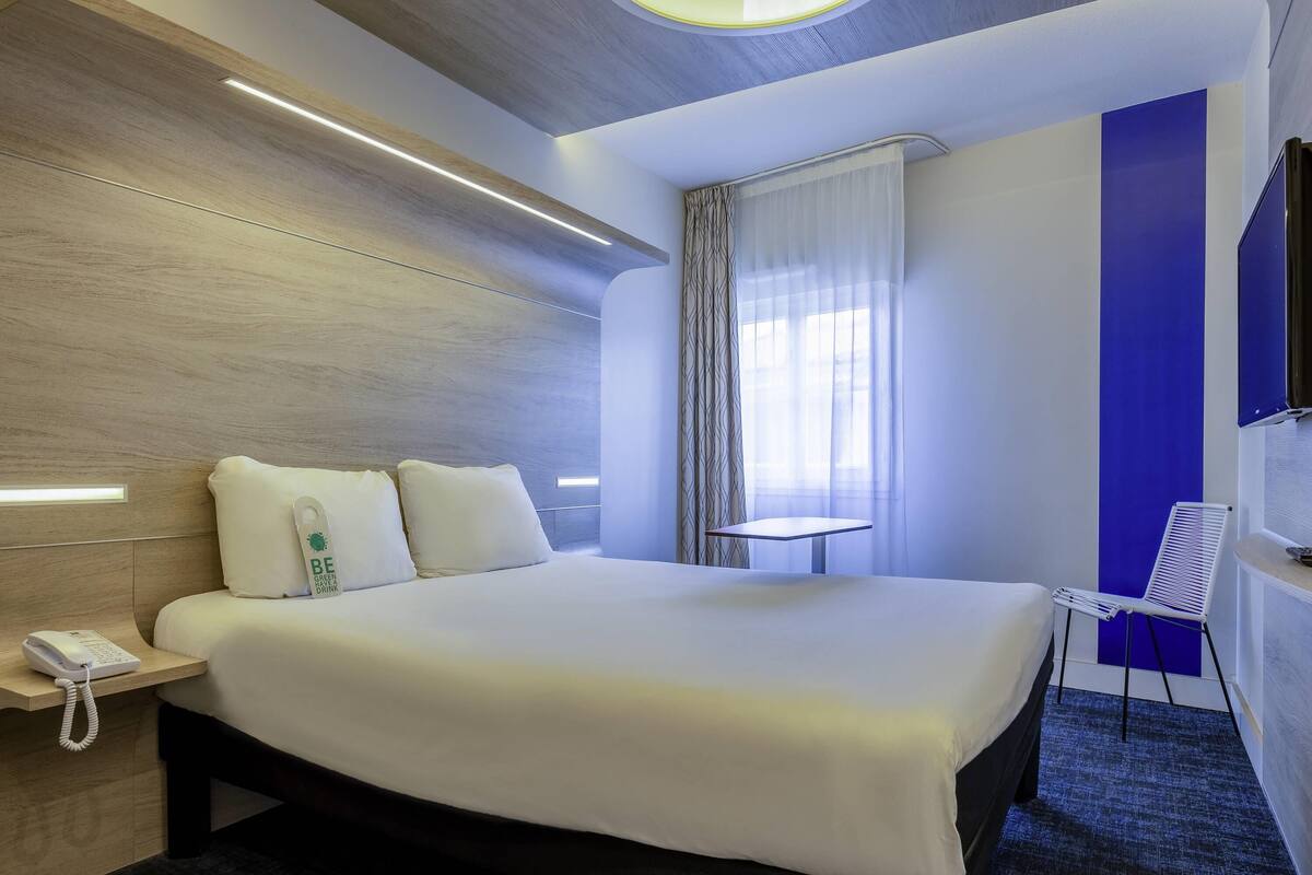 A hotel room with a large bed, bedside table with a phone, a small table, and a chair.
