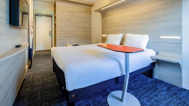 A modern hotel room with a bed, a TV mounted on the wall, and a carpeted floor. - ibis Styles La Rochelle Centre Vieux Port (La Rochelle)
