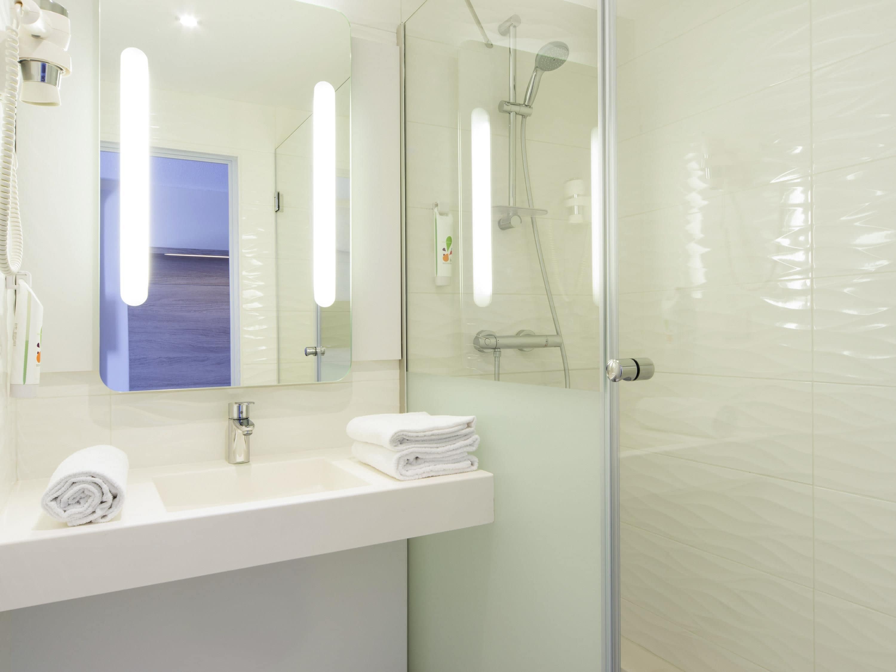Ein modernes Badezimmer mit Duschkabine aus Glas, einem weißen Waschbecken und einem beleuchteten Spiegel.