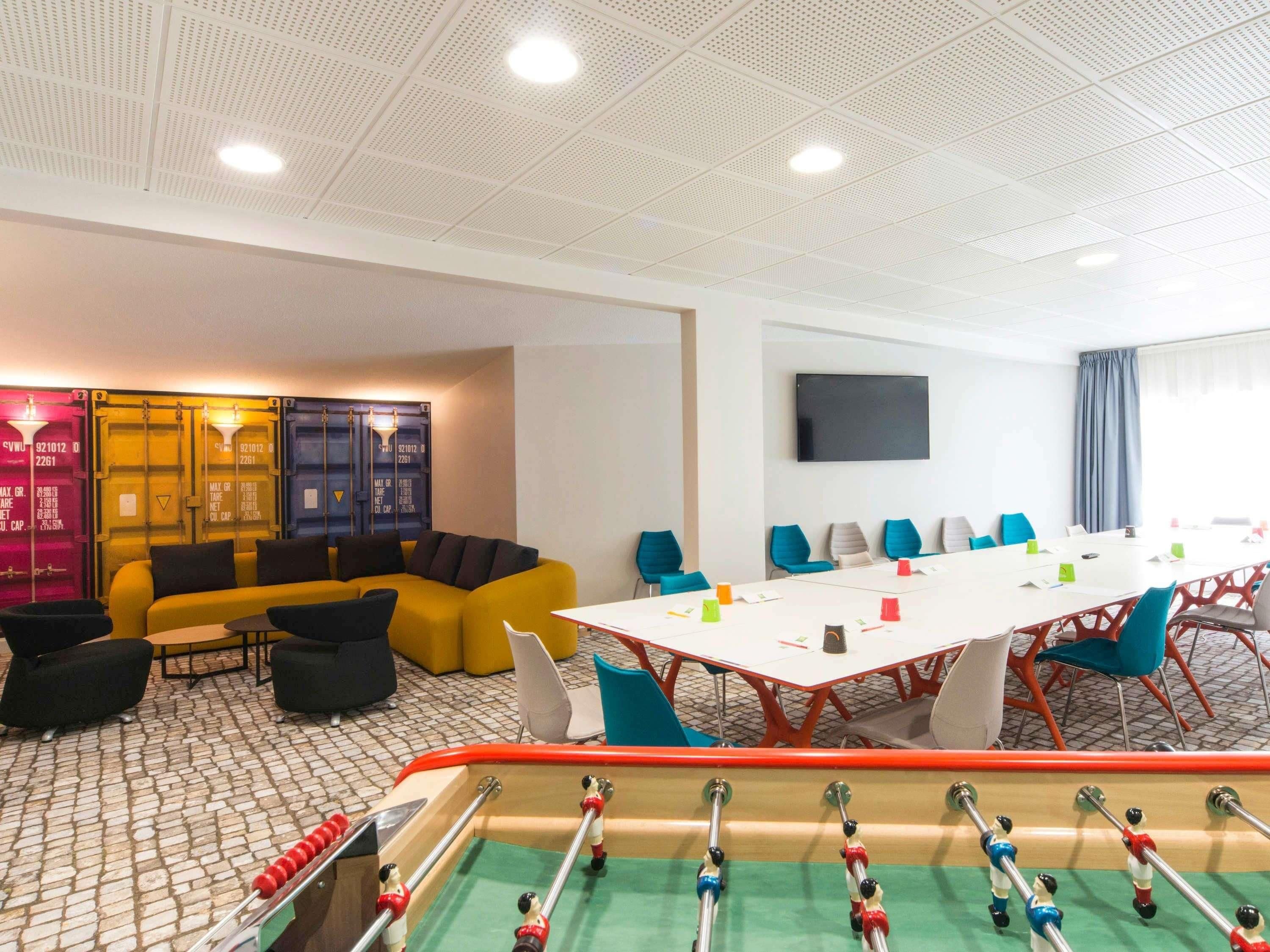 A conference room with a long table, chairs, a sofa, and a foosball table.