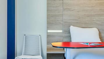 Una habitación de hotel moderna con una silla blanca, una mesita con una revista y una pared de acento roja.