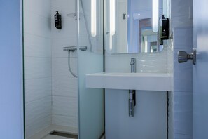 A modern bathroom with a glass shower enclosure, a white sink, and a mirror. - ibis Styles La Rochelle Centre Vieux Port (La Rochelle)
