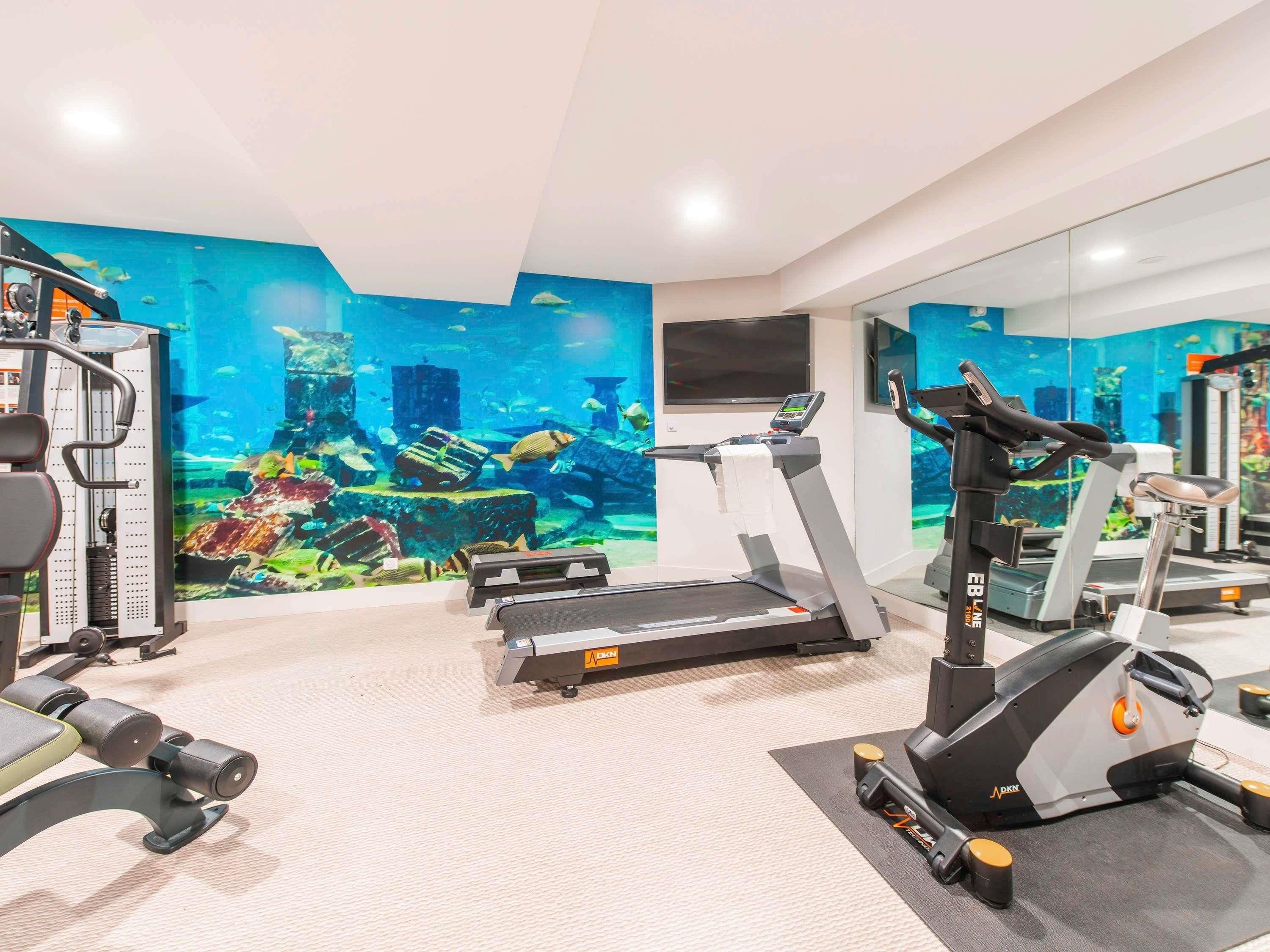 Ett gym med löpband, styrketräningsmaskiner och en väggmålning med undervattensmotiv.