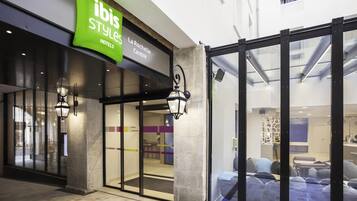 A hotel entrance with a green sign, glass doors, and a view into the interior.