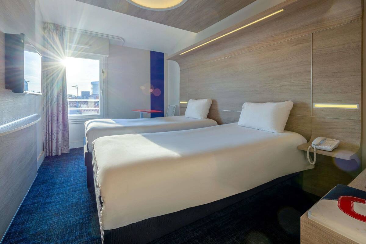 A hotel room with two beds, a desk with a phone, and a view of the city.