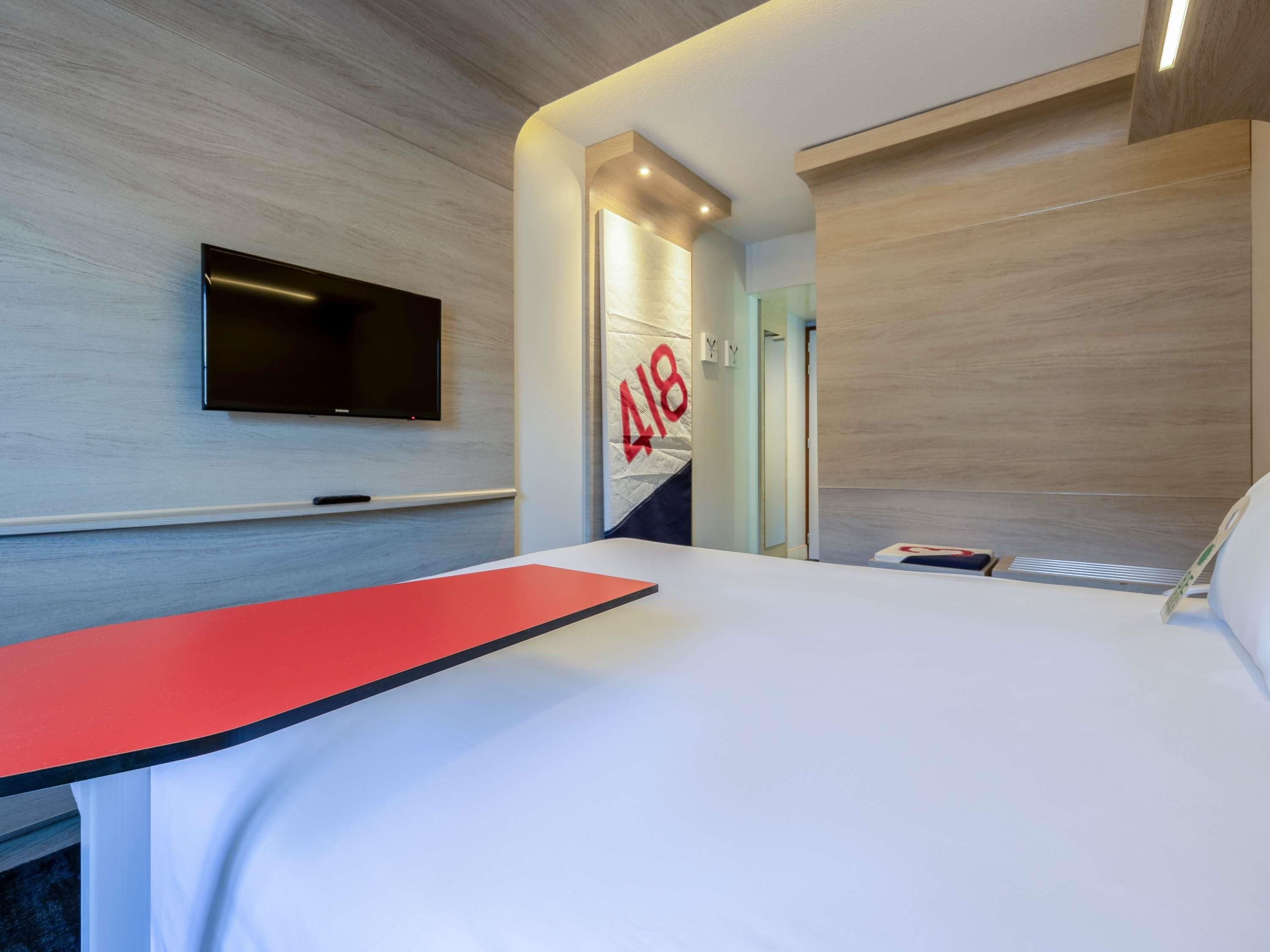 Una habitación de hotel con una cama, un televisor montado en la pared y una puerta con el letrero número 418 en rojo.