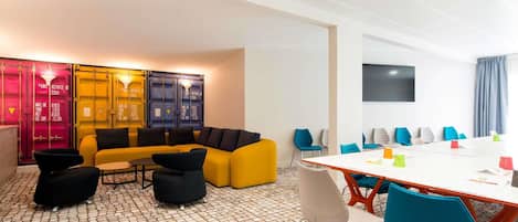 A modern meeting room with a white table, colorful chairs, and a yellow sofa.