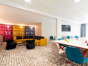 A modern meeting room with a white table, colorful chairs, and a yellow sofa.
