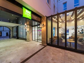 The exterior of an ibis Styles hotel with a glass entrance, a signboard, and a seating area visible through the glass. - ibis Styles La Rochelle Centre Vieux Port (La Rochelle)