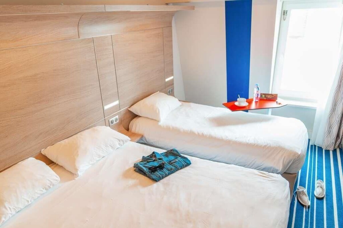 A hotel room with two beds, a wooden headboard, a window with curtains, and a striped floor.