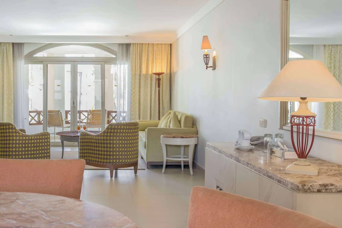 Une chambre d’hôtel comprenant un coin repas, un canapé, une télévision et un balcon avec des rideaux.