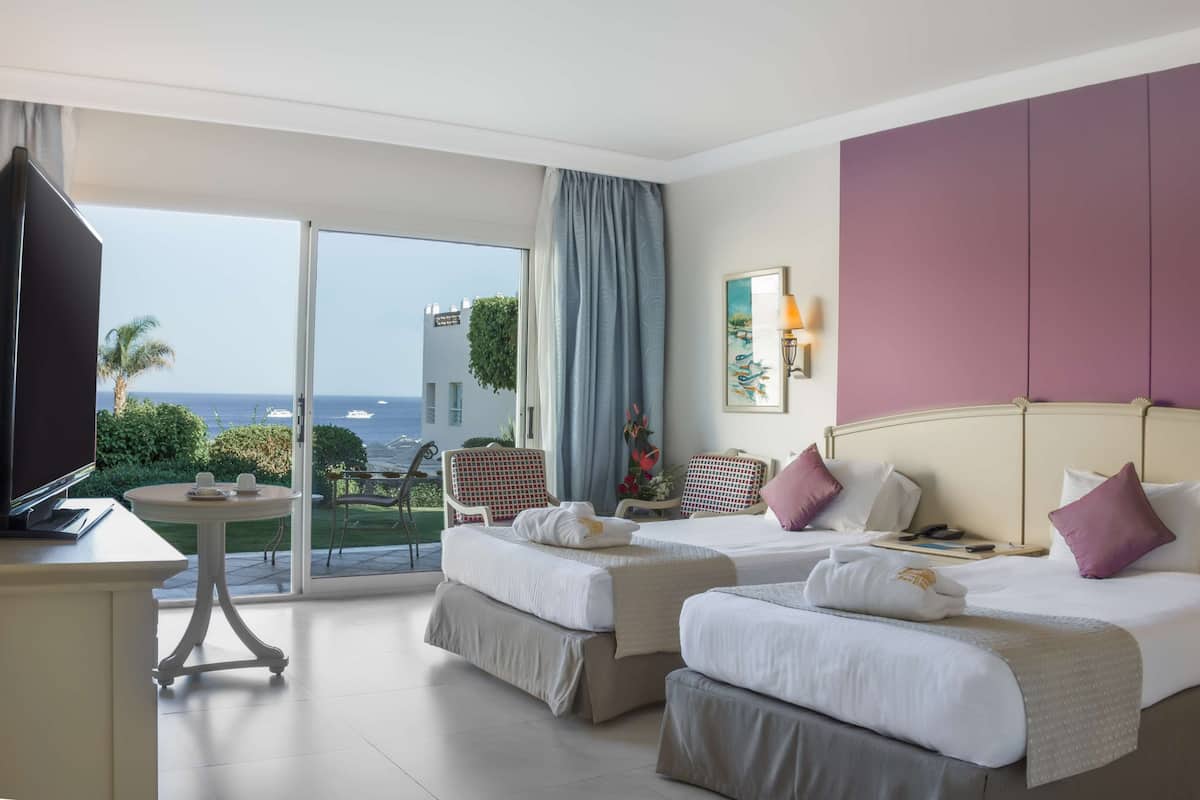 Une chambre d’hôtel avec deux lits, une télévision, un balcon donnant sur la mer et un coin repas.