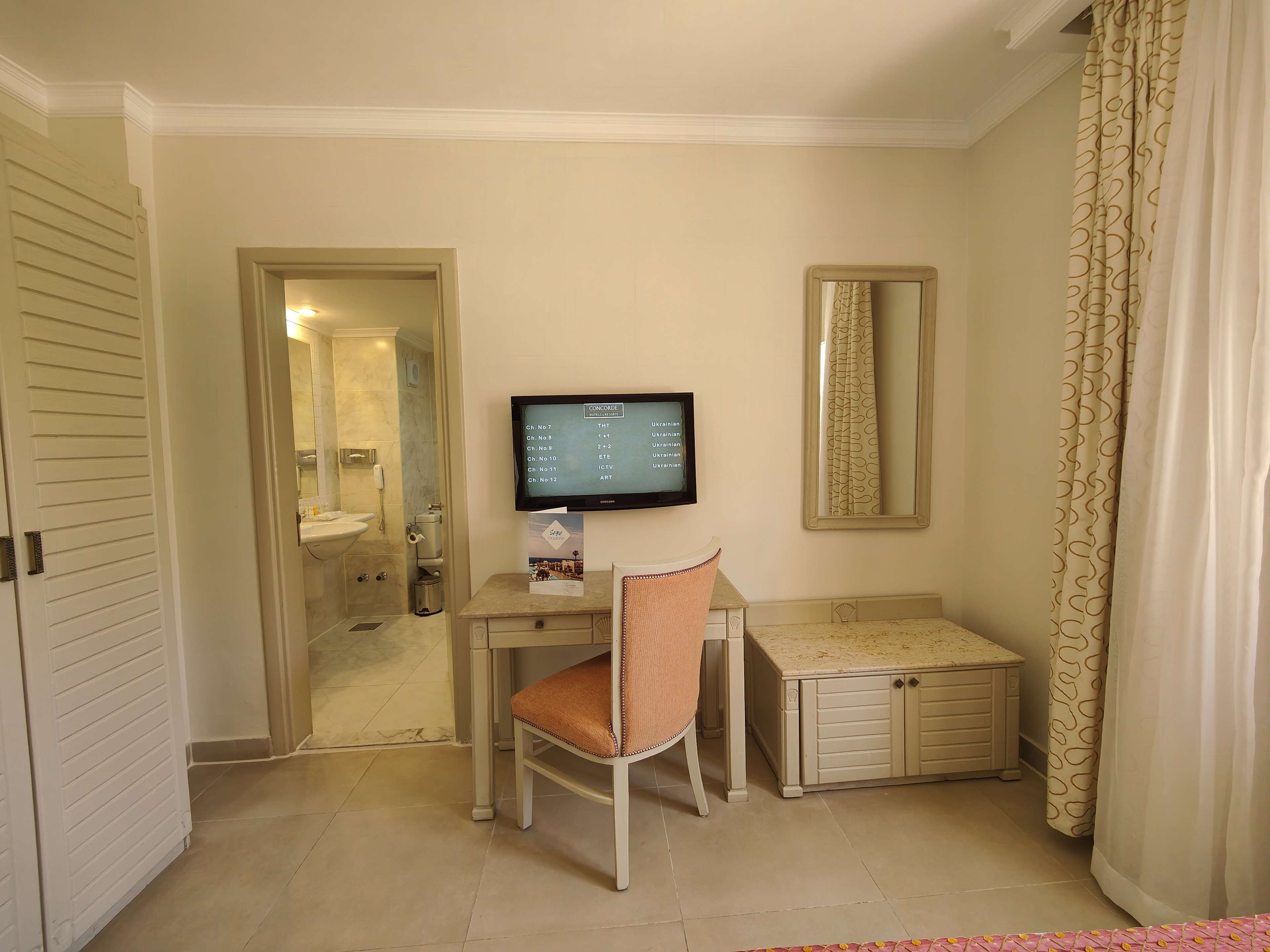 A hotel room with a desk, chair, and a television displaying a menu.
