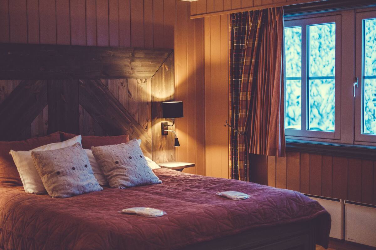A wooden-paneled bedroom with a large bed, a nightstand, and a window with curtains.