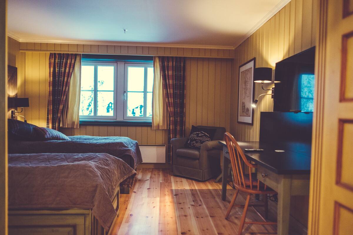 A room with two beds, a chair, a desk, and a window with curtains.