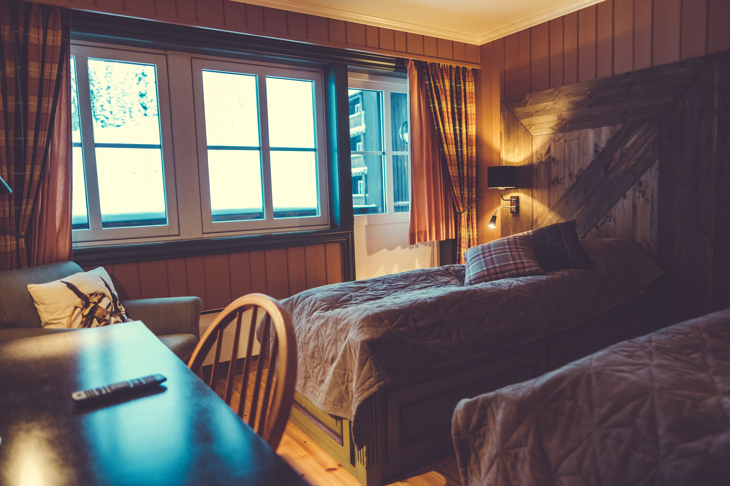 Ein Zimmer mit zwei Betten, einem Holztisch, einem Stuhl und einem Fenster mit Vorhängen.
