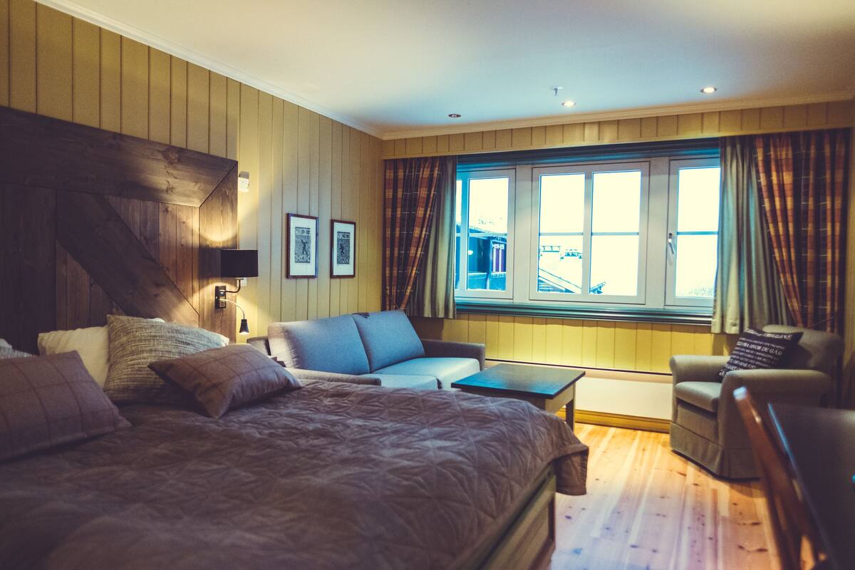 A bedroom with a large bed, a sofa, a small table, and a window with curtains.