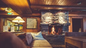 Une pièce chaleureuse avec une cheminée en pierre, des murs en bois, un canapé et une table.