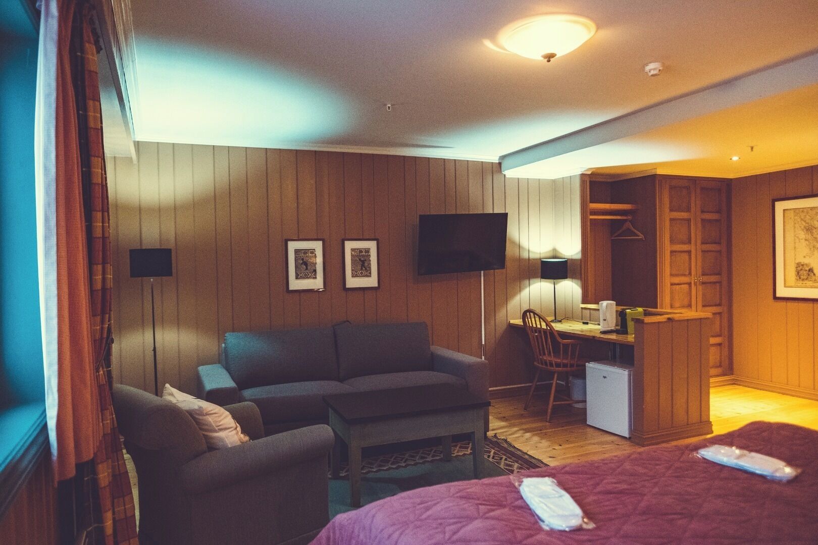 A hotel room with a sofa, a desk, a chair, a bed, and a television.