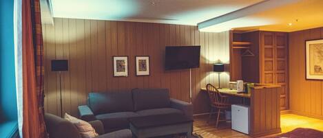 A hotel room with a sofa, a desk, a chair, a bed, and a television.