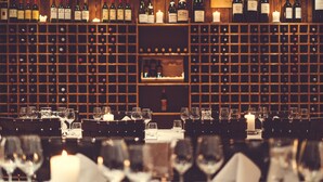 Un restaurant doté d’une cave à vin, de tables décorées avec des verres et des bougies, et d’un bar où sont exposées des bouteilles.