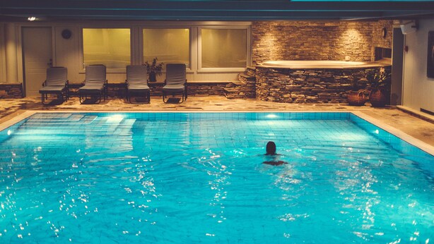 Une piscine avec une personne qui nage, des chaises longues et un mur en pierre.
