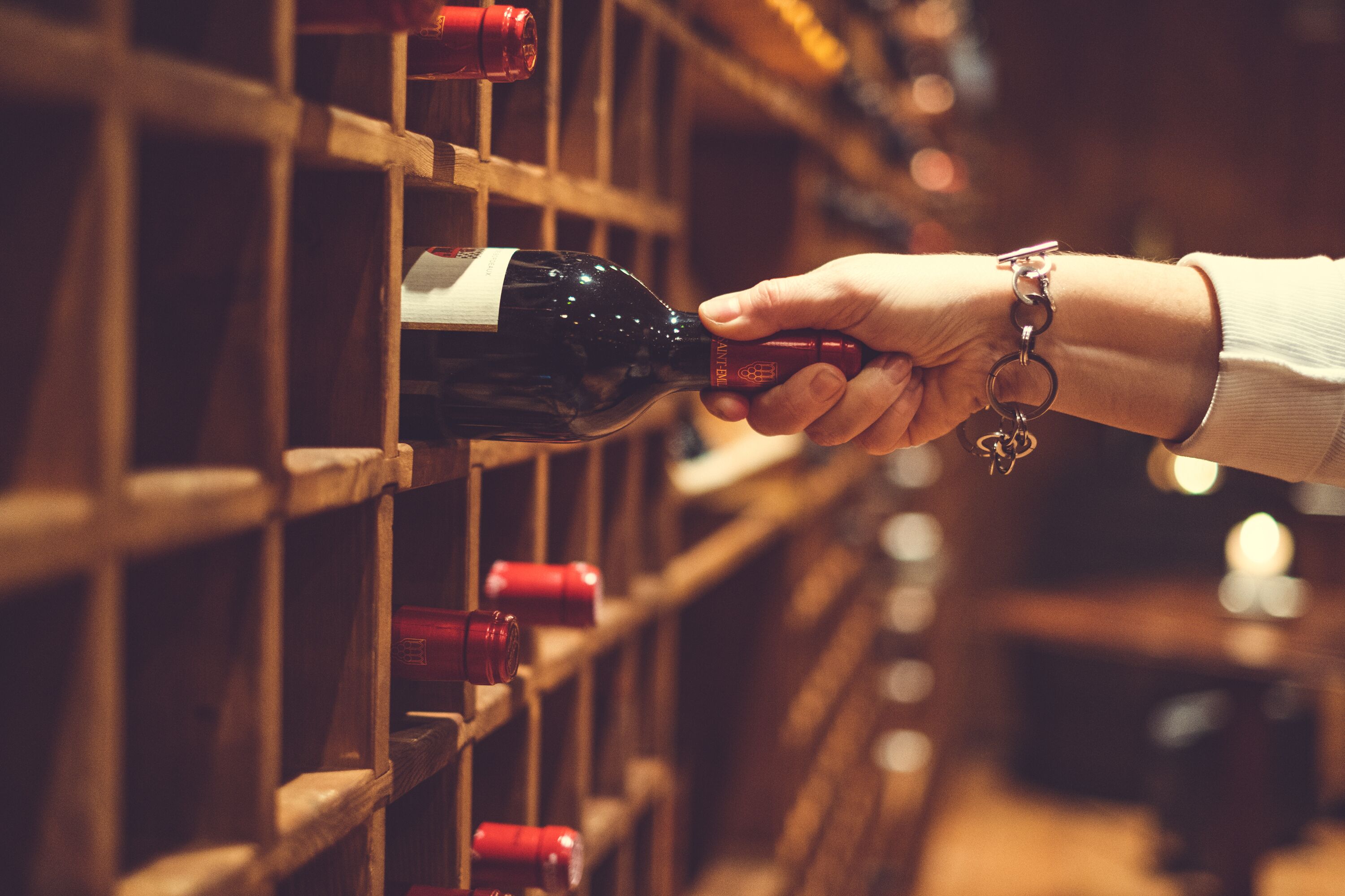 Una mano sostiene una botella de vino, alcanzando otra en un estante de madera.