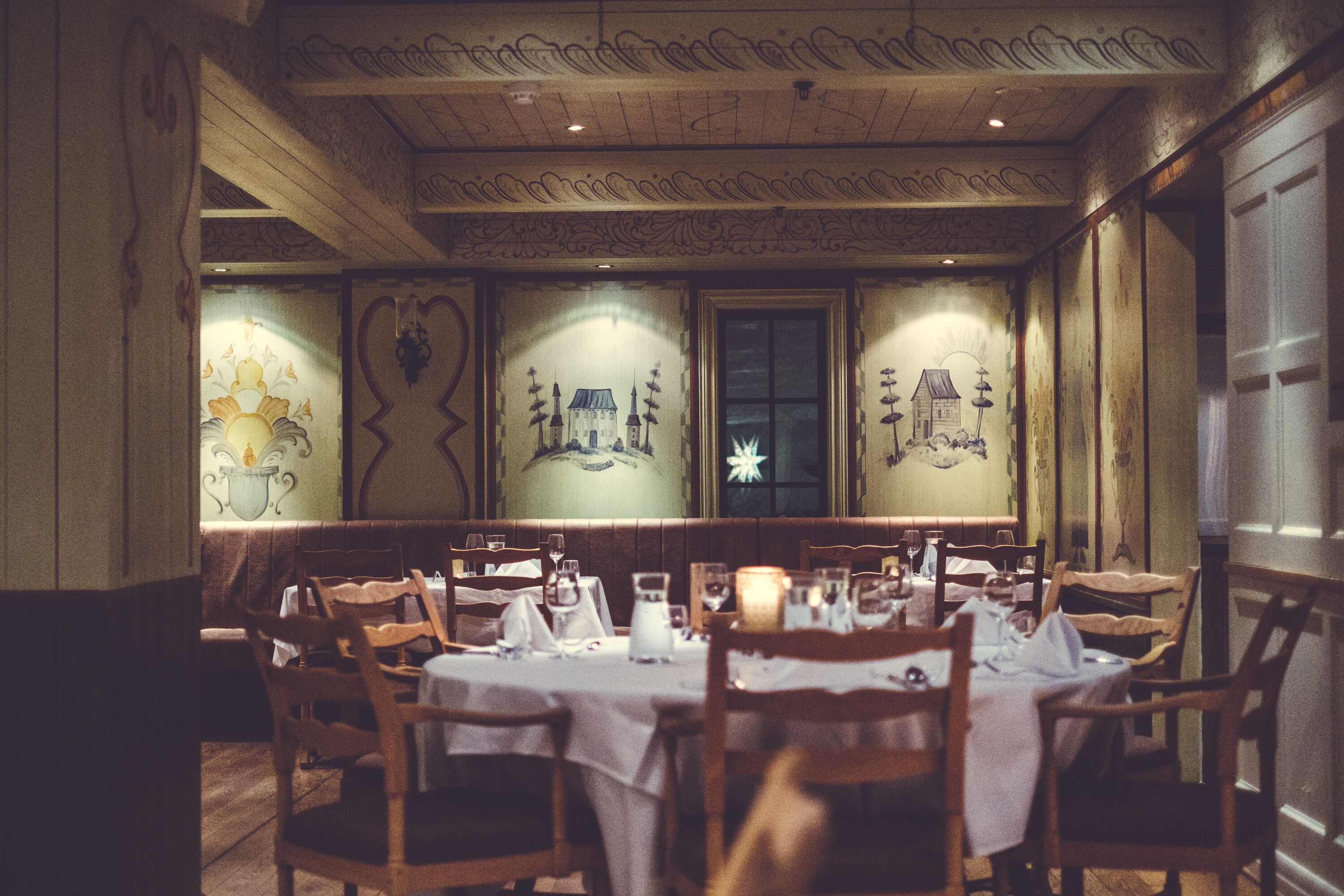 A dining area with wooden tables and chairs, ornate wall decorations, and a chandelier.