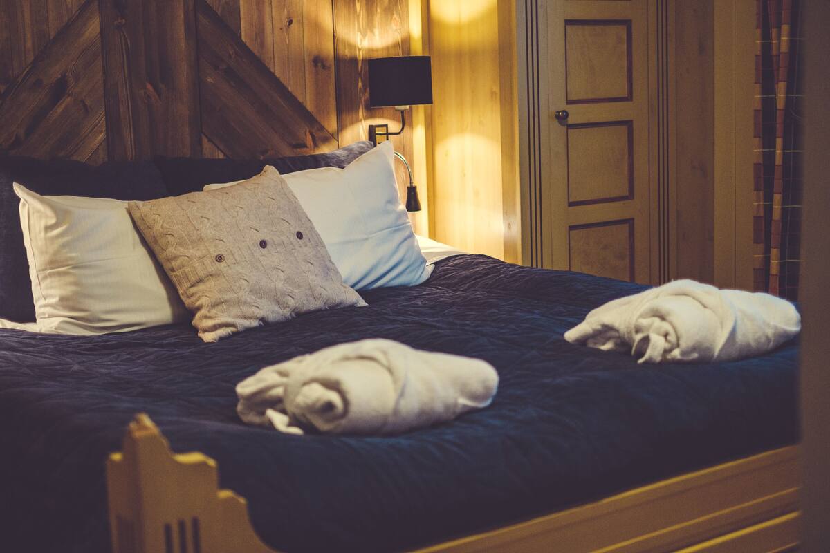 A neatly made bed with pillows and towels, a wooden headboard, a bedside lamp, and a door with a window.
