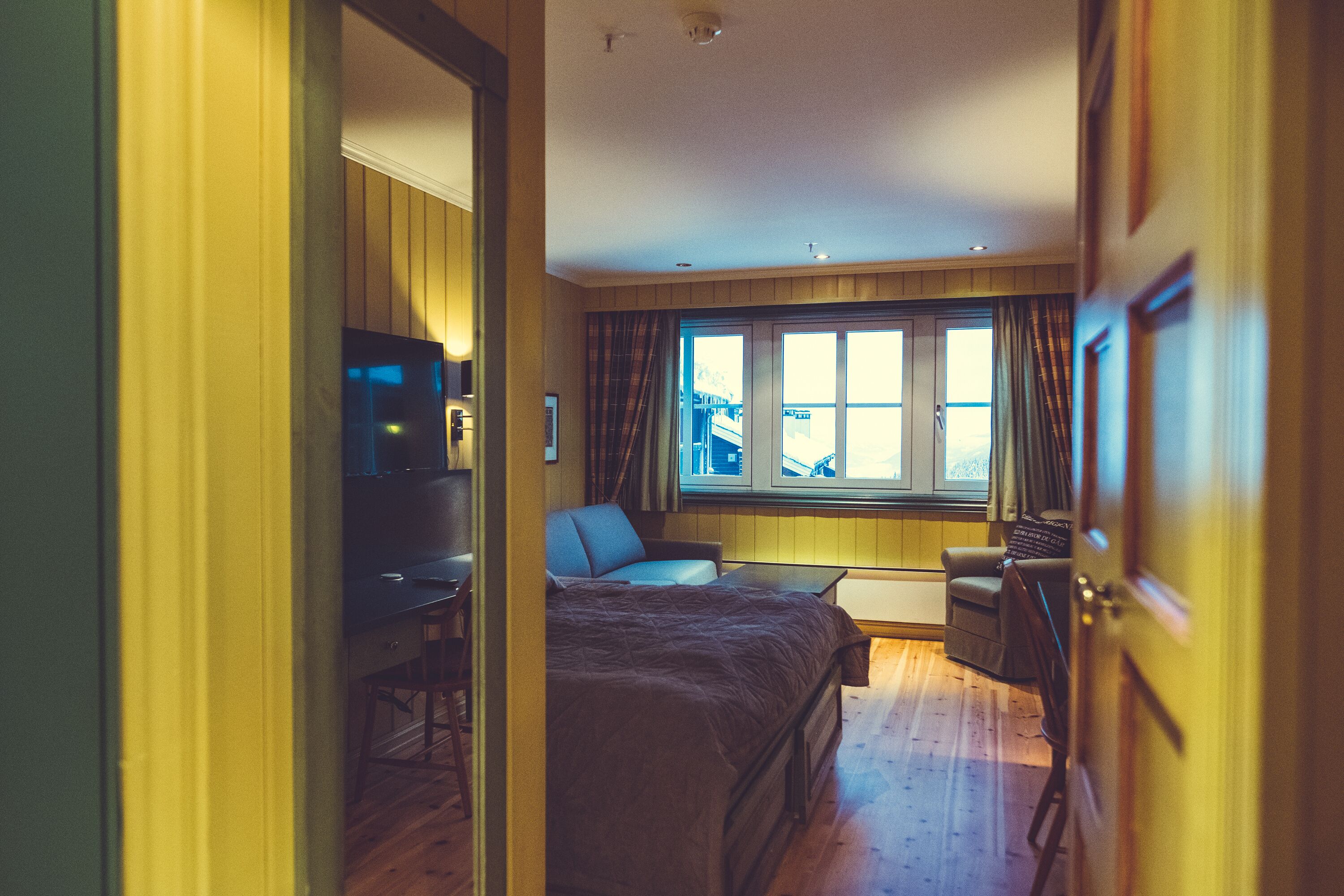 Habitación de hotel con cama, escritorio y silla. Cuenta con ventana con cortinas y vistas al exterior.