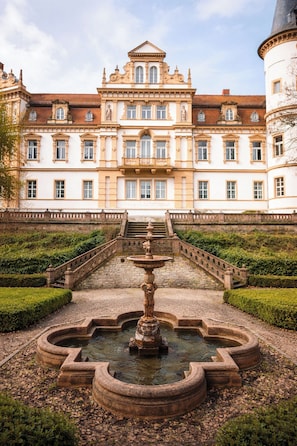 A grand building with a central fountain, symmetrical gardens, and a staircase leading to the entrance.