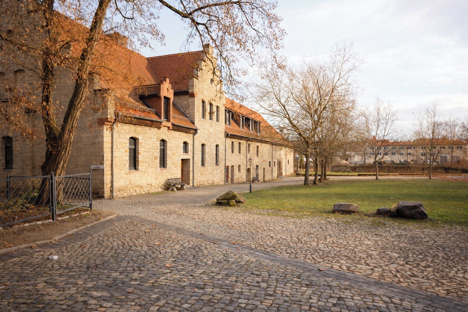Un bâtiment historique en pierre, doté d’une cour, d’un chemin pavé et d’un banc.