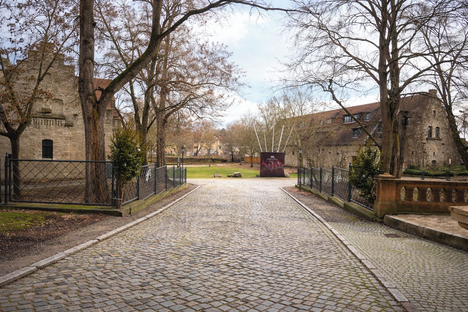 Ein Pflasterweg führt zu einem historischen Gebäude mit Steinmauern und einem Metallgitter.