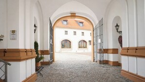 A cobblestone corridor with white walls and wooden trim, leading to a building with arched windows and a tiled roof. - Schlosshotel Schkopau (Schkopau)
