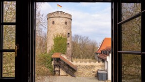 A view of a stone tower with a flag, a staircase leading to a building, and a cobblestone path. - Schlosshotel Schkopau (Schkopau)