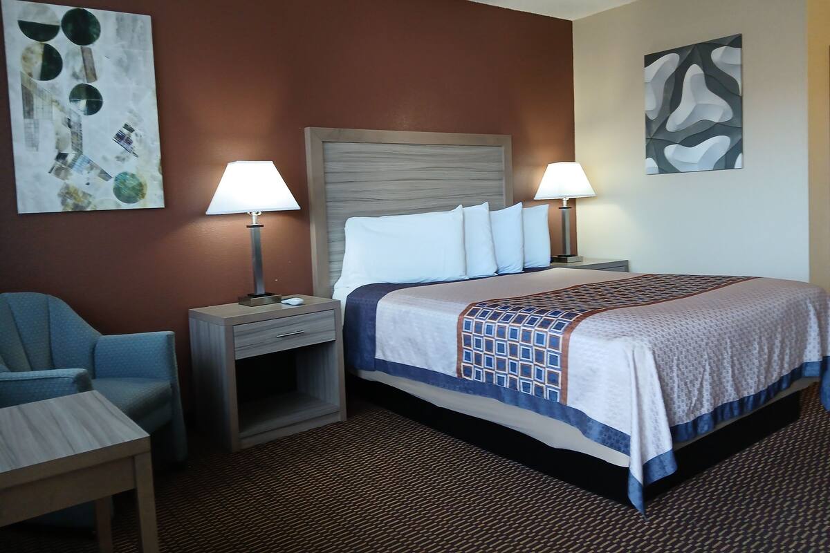 A hotel room with a bed, two bedside tables with lamps, a chair, and artwork on the walls.